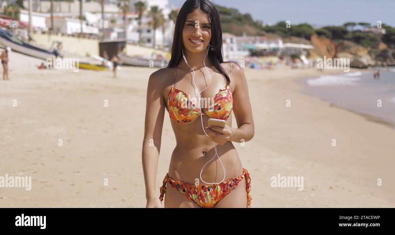 Una mujer en bikini blanco se encuentra en una playa y mira a la cámara.