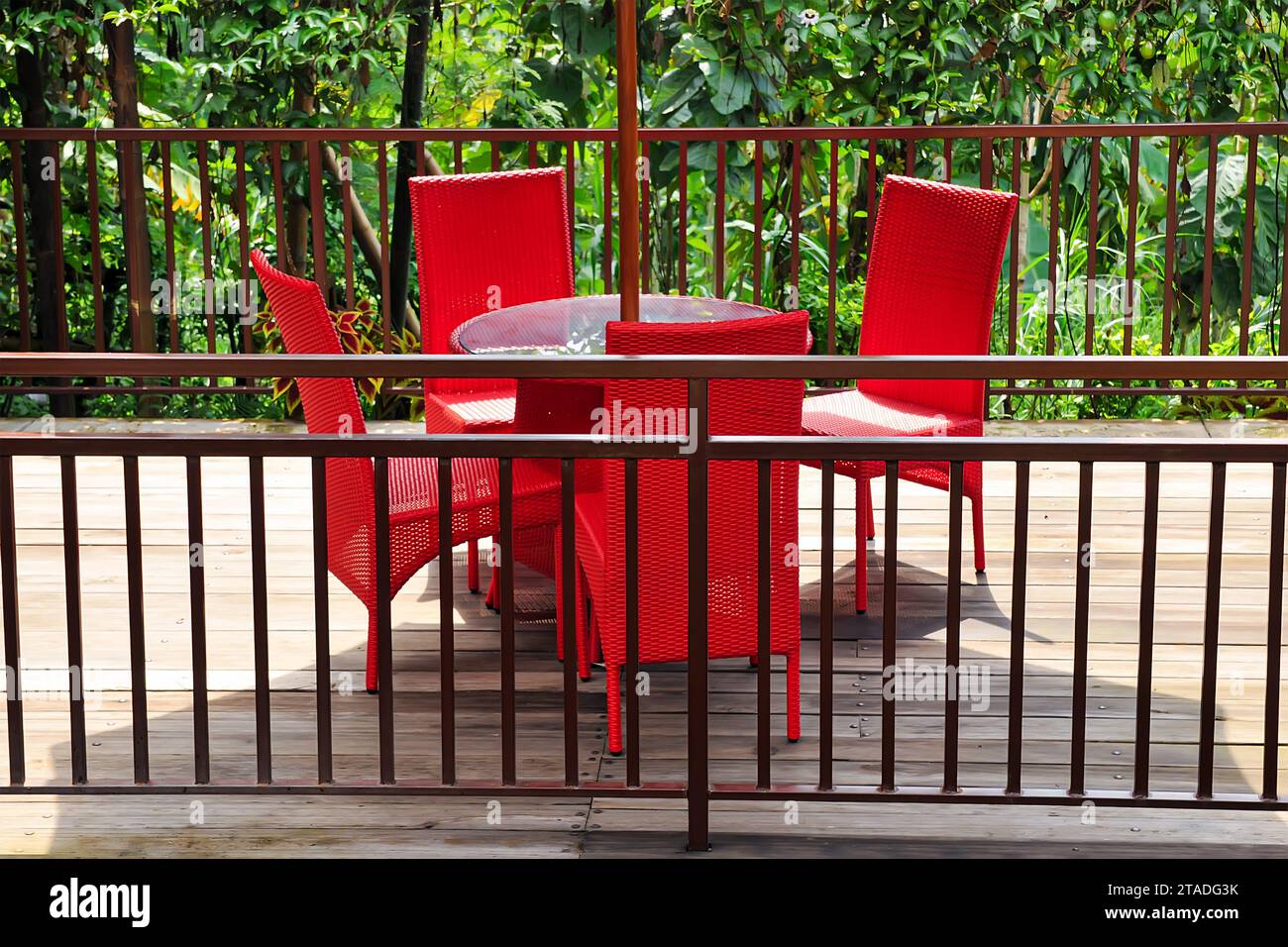 Cenador de jardín con una mesa de vidrio y sillas tejidas rojas con una valla de enrejado y paraguas Foto de stock