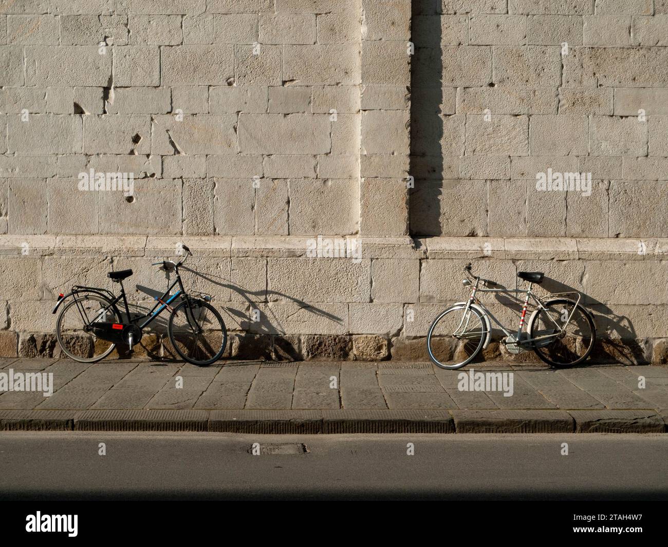 Dos bicicletas frente a la otra contra la pared de piedra de una iglesia italiana en el sol de verano Foto de stock