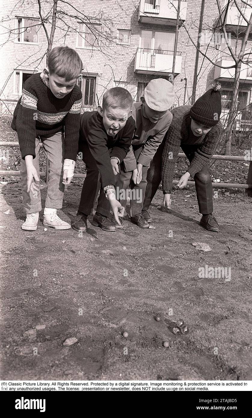 En la década de 1960 Niños al aire libre jugando canicas. Un juego anticuado donde el objetivo es golpear la pirámide de mármoles con un solo mármol. Si golpeas, ganaste los mármoles en la pirámide, de lo contrario el mármol se perdió. También había variantes del juego. Suecia primavera de 1964. Roland Palm ref pärm 2. Foto de stock