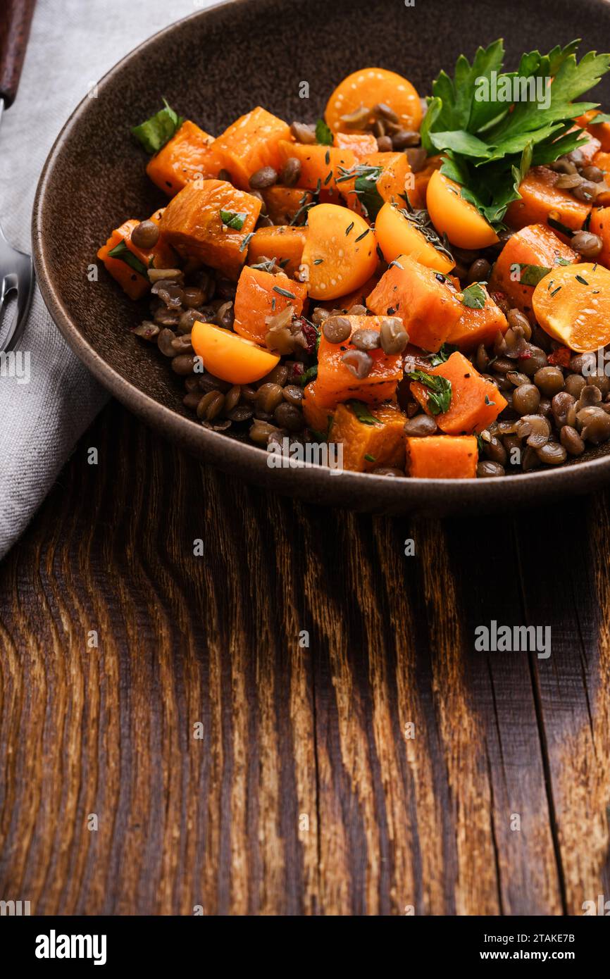 Comida vegana saludable, ensalada caliente de invierno con batatas asadas, lentejas, berris dorado y hierbas en un tazón de cerámica en una mesa de madera rústica, de cerca Foto de stock