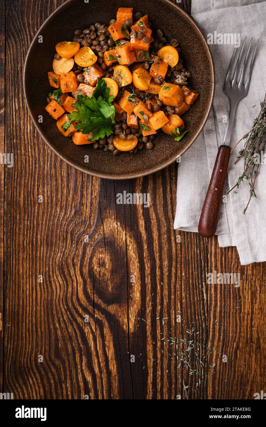 Comida vegana saludable, ensalada caliente de invierno con batatas asadas, lentejas, berris dorado y hierbas en un tazón de cerámica en una mesa de madera rústica, directamente Foto de stock