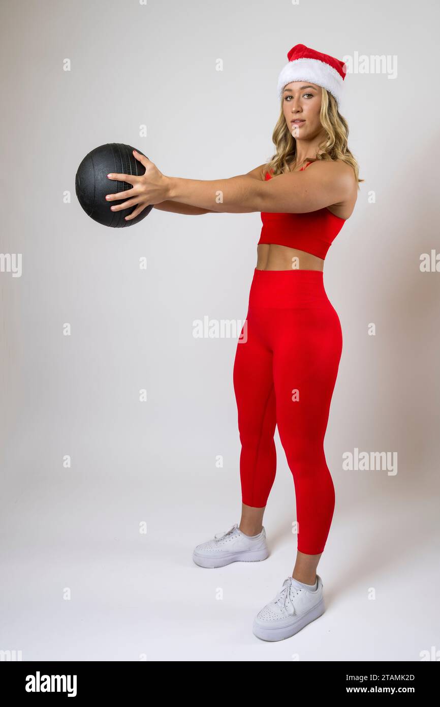 Bodybuilder Femenino Leggings Rojos y Deportes Sujetador Santa Hat Xmas Trabajando Bola de Medicina Foto de stock