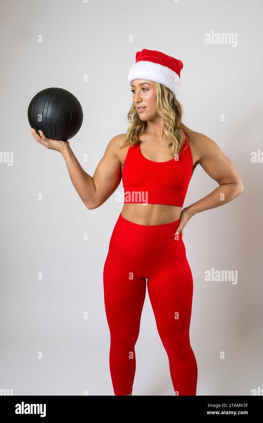 Bodybuilder Femenino Leggings Rojos y Deportes Sujetador Santa Hat Xmas Trabajando Bola de Medicina Foto de stock