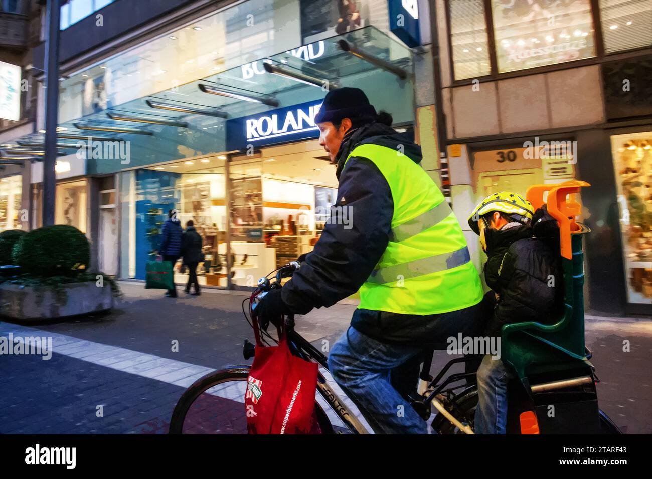 11-25-2015 Düsseldorf GERMEN Hombre joven en traje amarillo brillante que se mueve en bicicleta con el hijo en una silla especial - de la etnia de Asia oriental Foto de stock