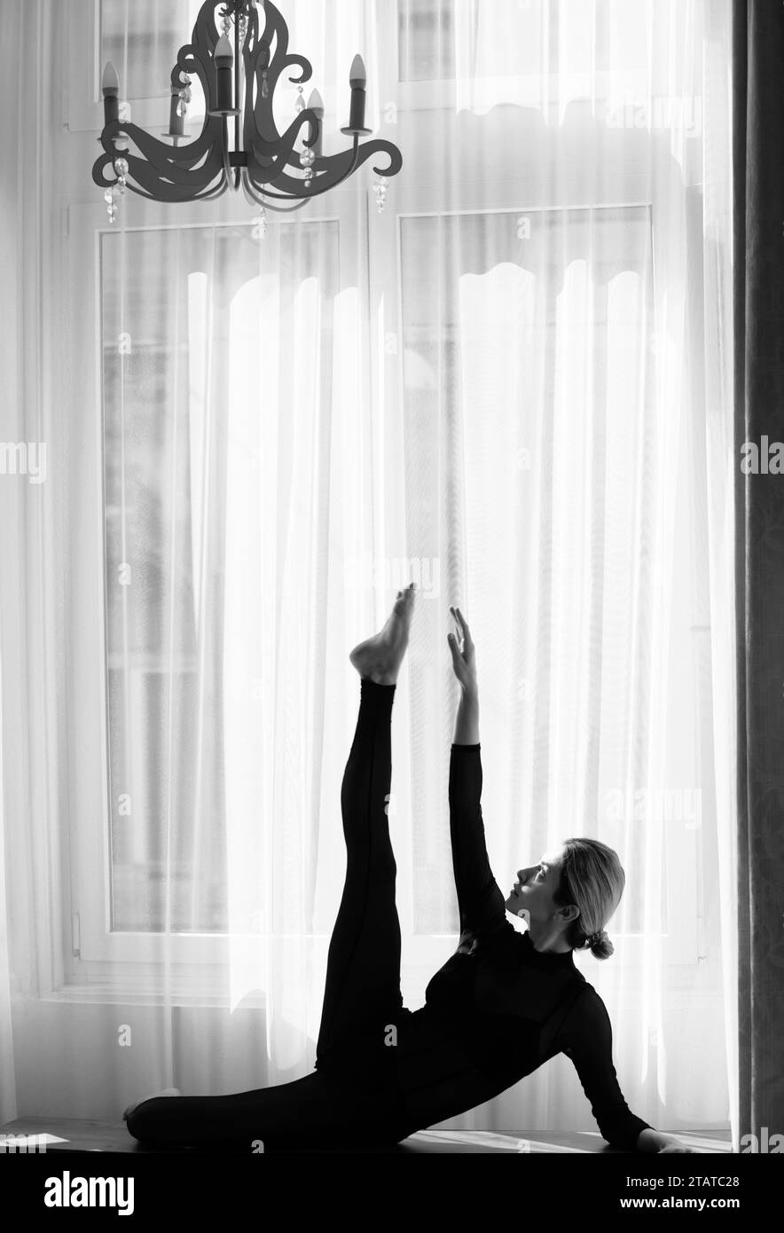 Mujer joven que se estira en casa cerca de la ventana. Chica joven deportiva haciendo ejercicio físico, vida sana. Foto de stock