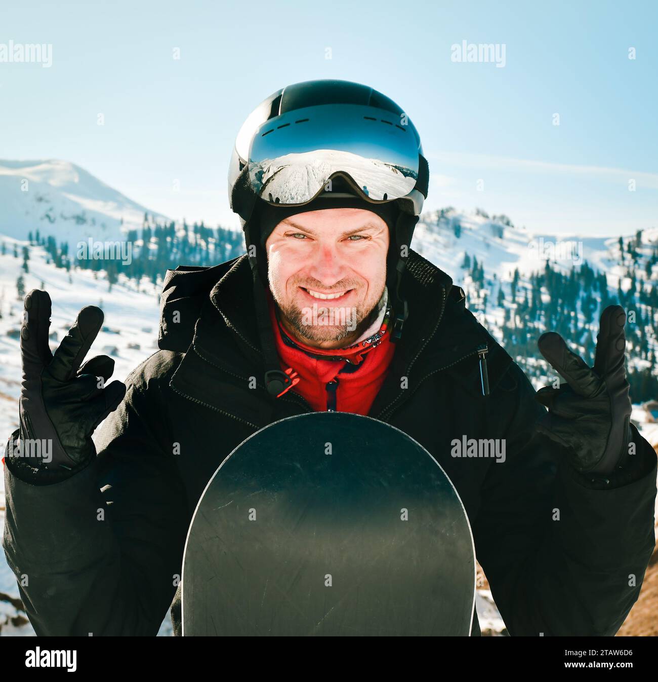 Hombre de snowboarder caucásico con gafas de esquí y equipo de esquí de colores, mostrando los pulgares hacia arriba en la pendiente Foto de stock