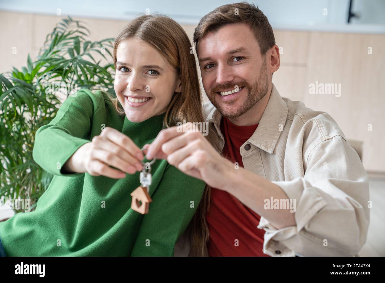 Los cónyuges jóvenes compraron bienes raíces sosteniendo llaves en manos sonriendo mirando a la cámara. Foto de stock