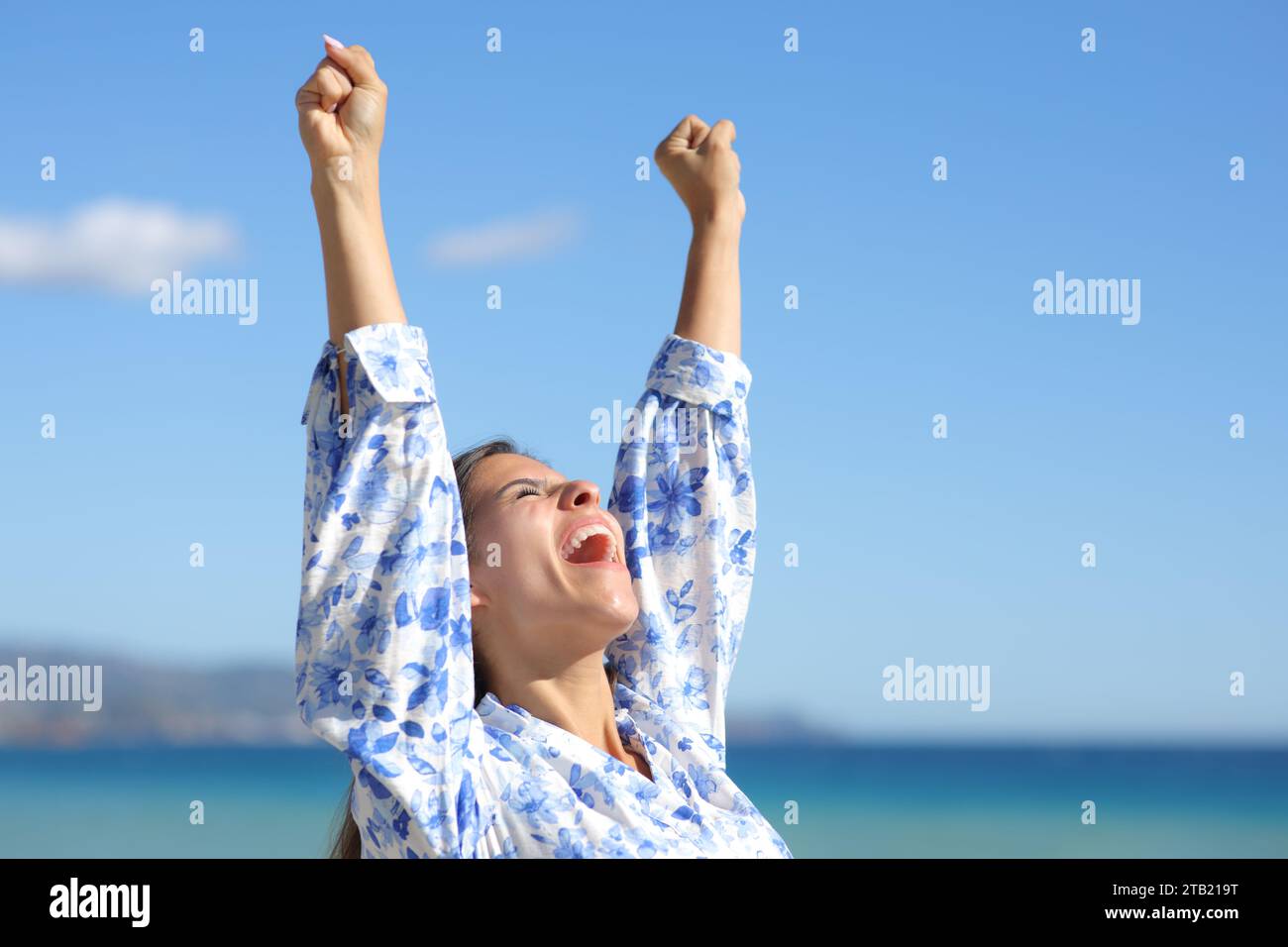 Mujer emocionada levantando los brazos en la playa celebrando el éxito Foto de stock