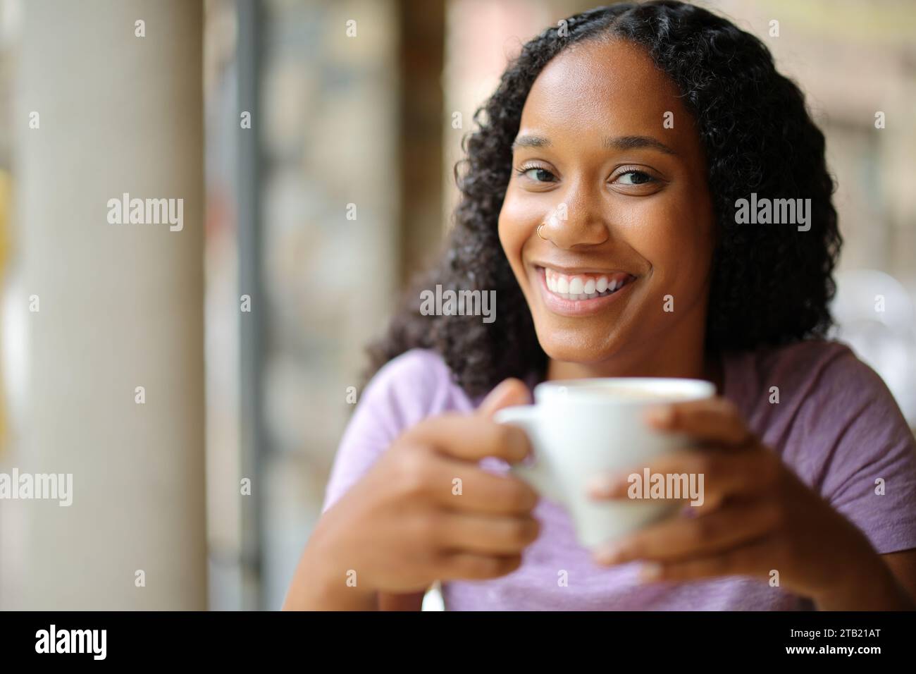 Mujer negra feliz bebiendo café mirando a la cámara en una terraza del bar Foto de stock