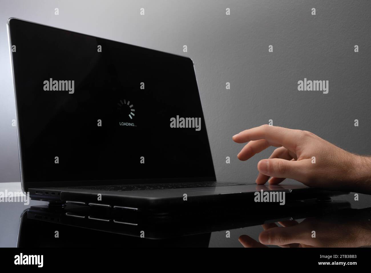 Un hombre impaciente tocando sus dedos esperando una pantalla de carga en una computadora portátil. Foto de stock