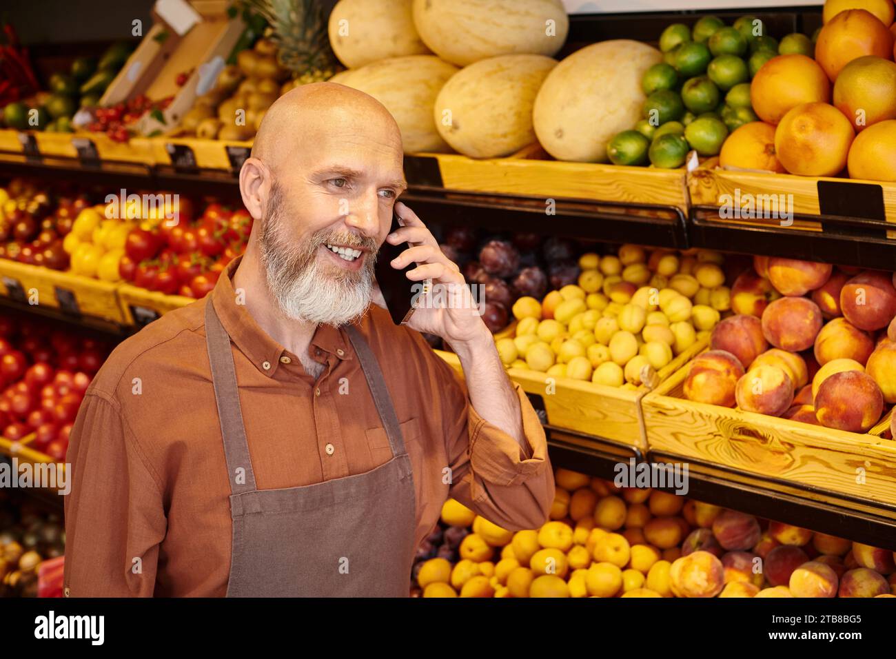 vendedor maduro de buen aspecto con barba hablando por teléfono mientras que en el descanso de trabajar en la tienda de comestibles Foto de stock