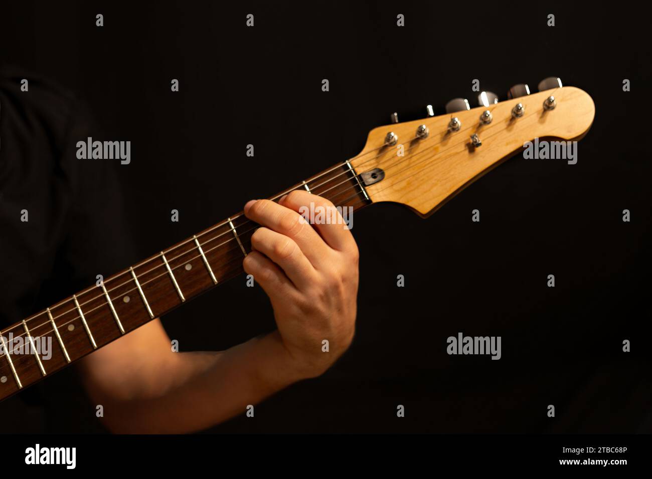 Músico tocando la guitarra en concierto con un fondo negro detrás de él Foto de stock