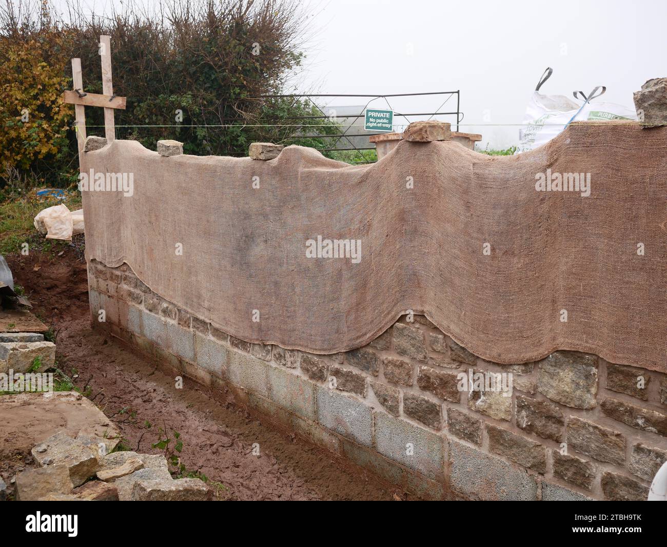 Muro fronterizo con orientación de piedra tradicional que se está construyendo en un nuevo desarrollo de propiedad. Hessian protege el nuevo ladrillo del frío. Foto de stock