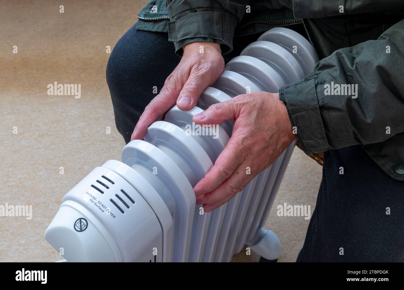 Una persona sentada en una habitación abrazando un calentador eléctrico portátil tratando de mantener el calor en el frío del invierno. Foto de stock