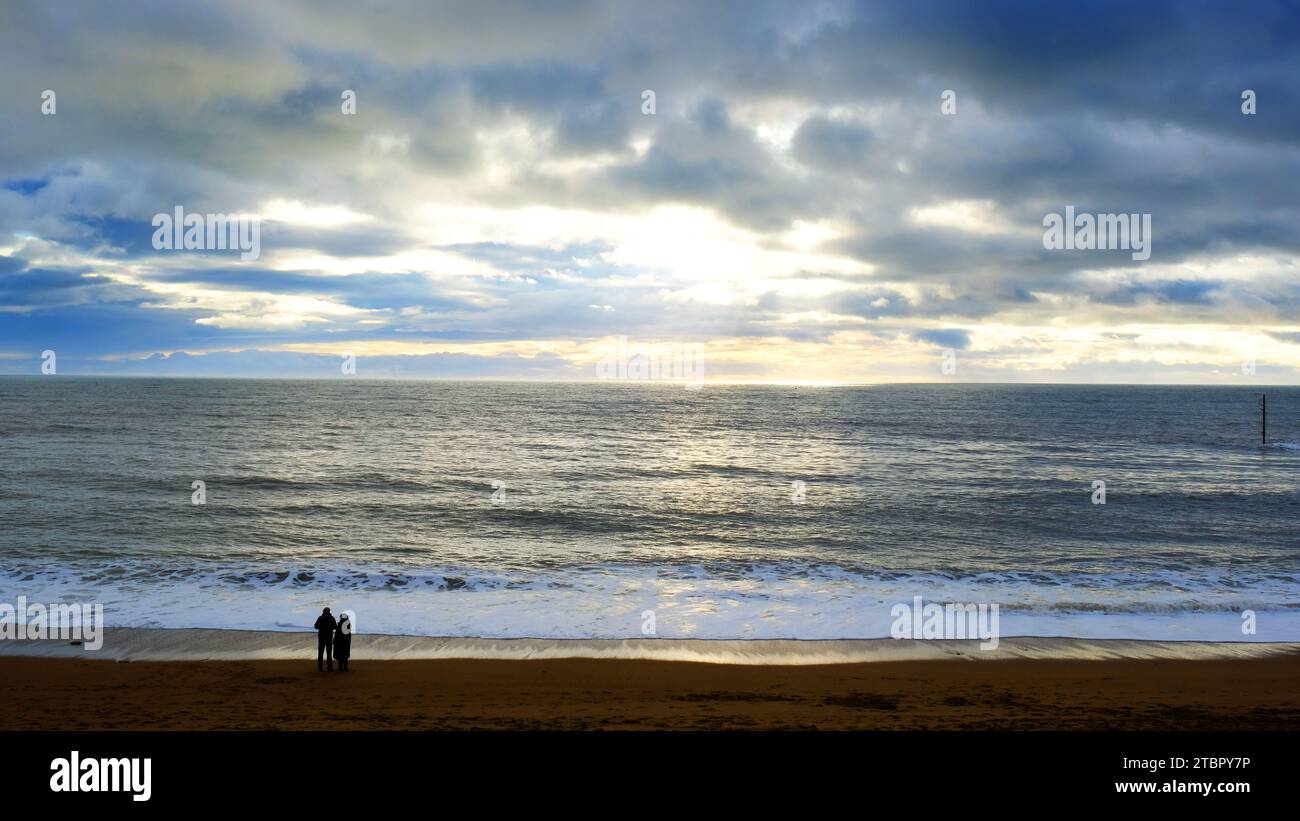 Pareja sola en la playa admirando una puesta de sol - John Gollop Foto de stock