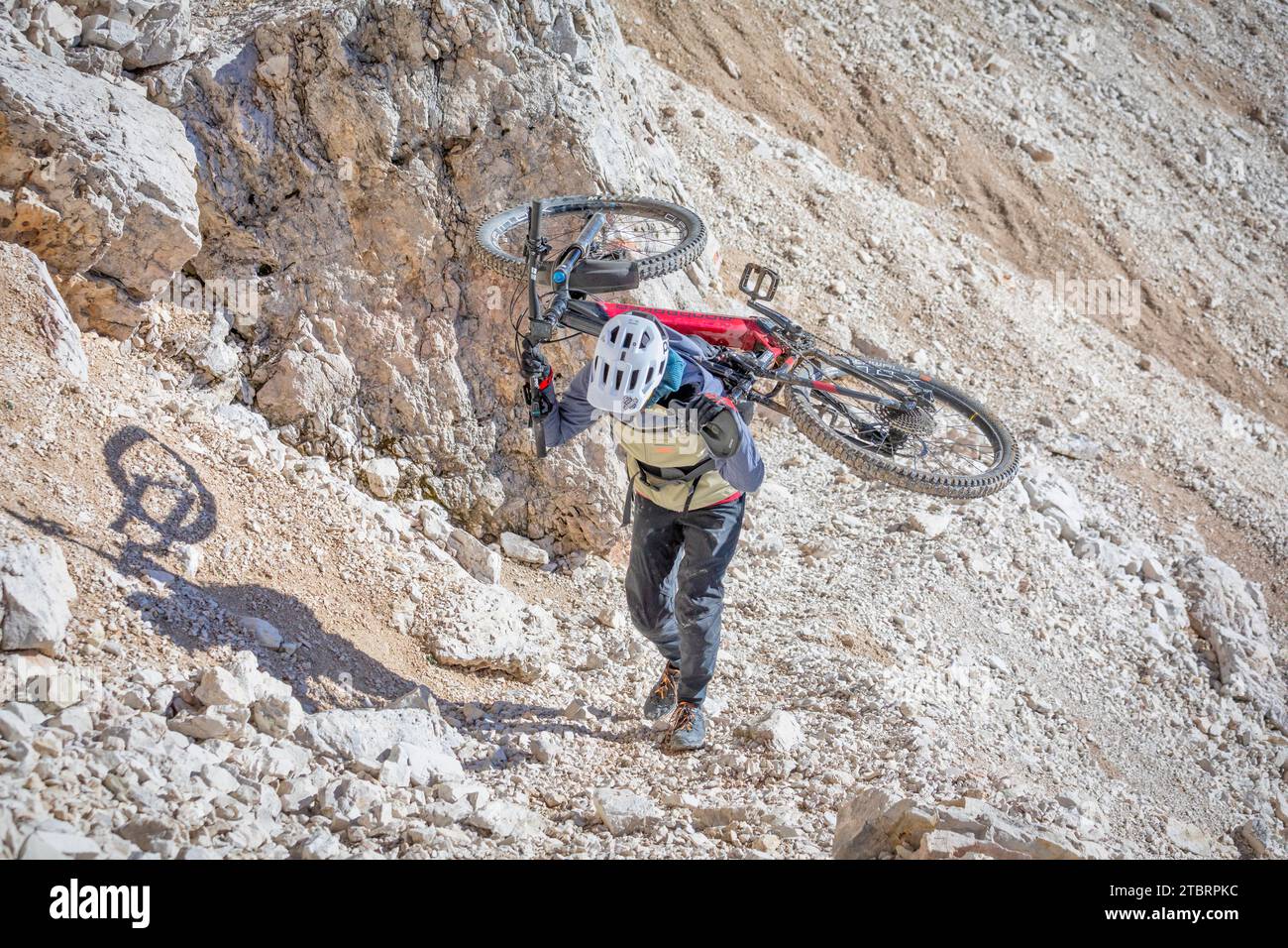 Italia, Dolomitas, ciclista de montaña en un sendero alpino llevando la bicicleta de montaña en su espalda en una sección muy difícil Foto de stock