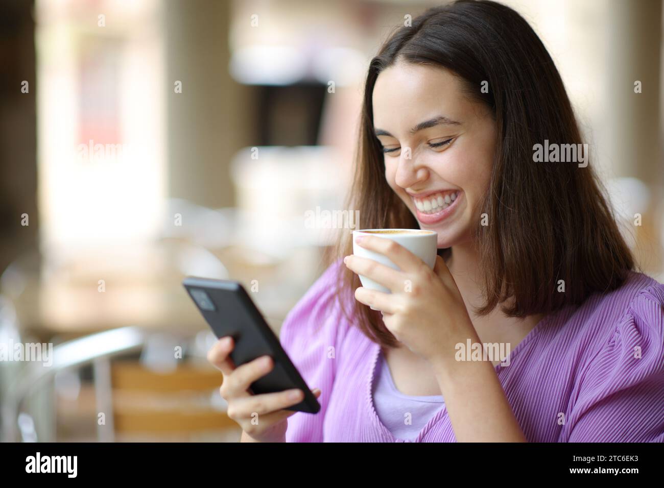Mujer feliz bebiendo café usando el teléfono celular en una terraza del bar Foto de stock