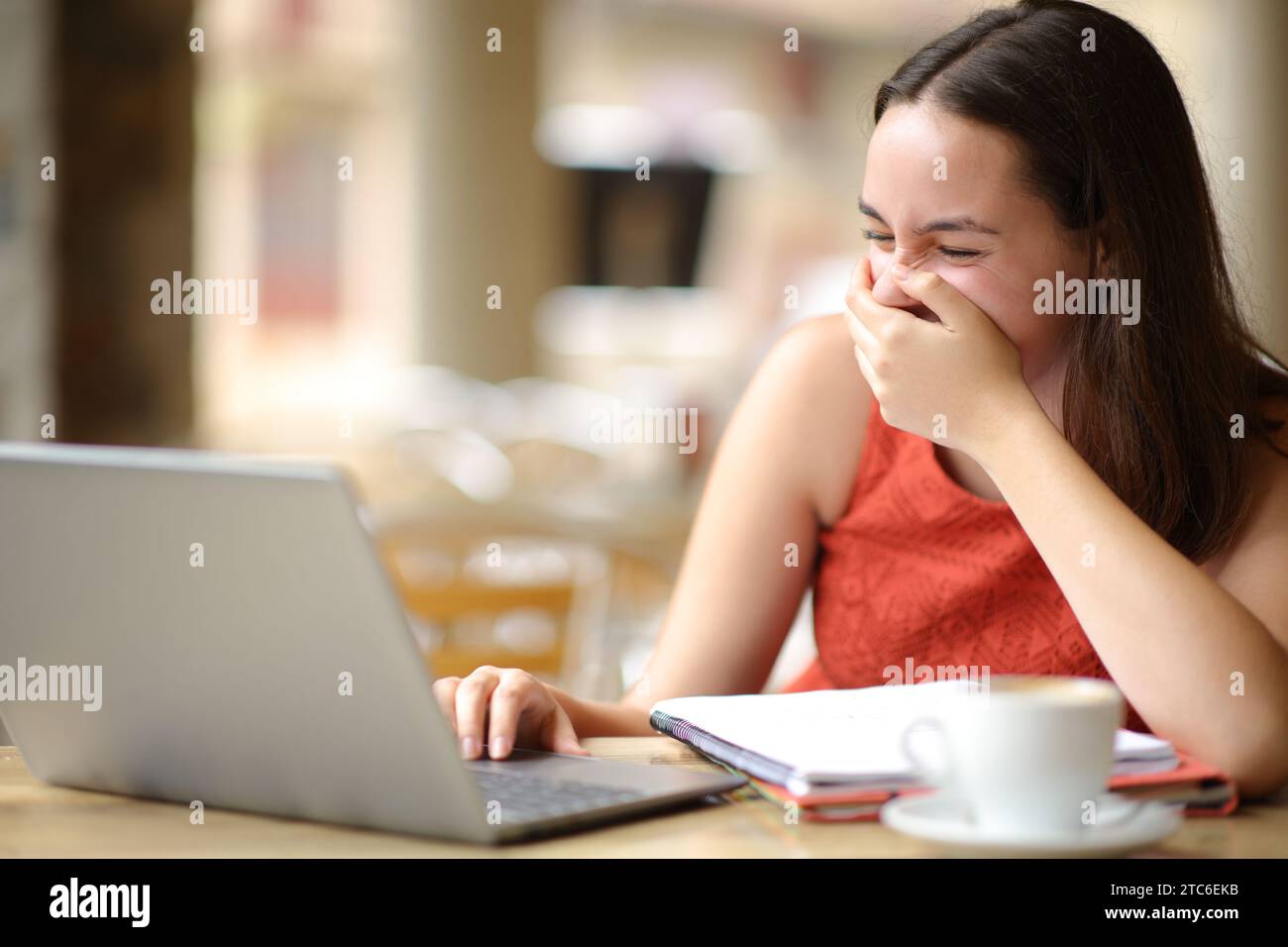 Estudiante feliz riendo fuerte viendo los medios de comunicación en el ordenador portátil en una terraza de la cafetería Foto de stock