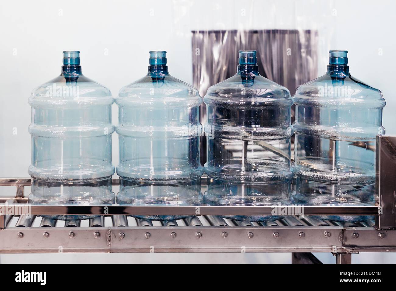 botellas limpias de agua potable se mueven automaticamente en rodillos transportadores para regar el embotellado en la fábrica de plantas de agua potable. Foto de stock