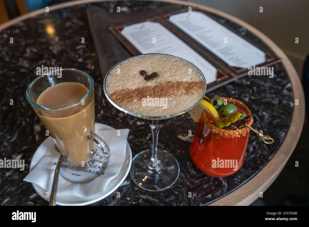 Tres cócteles de lujo en la mesa de mármol con menú de bebidas borrosas en el fondo Foto de stock