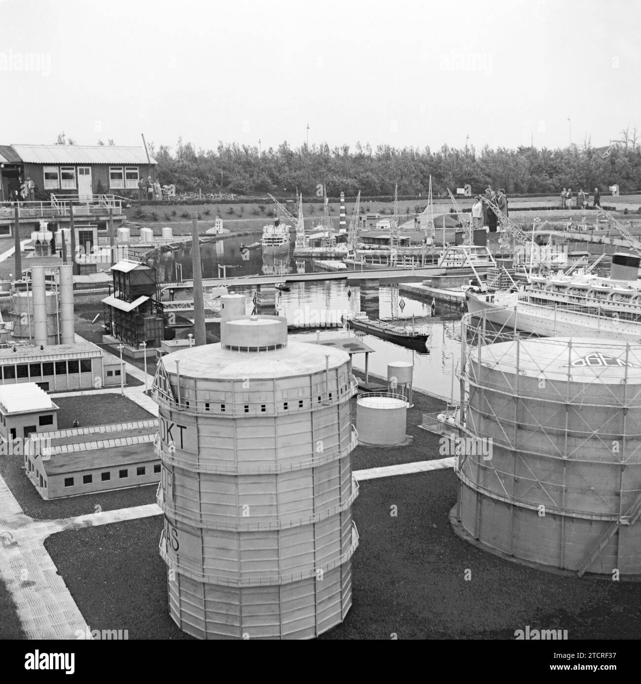 Madurodam, La Haya, Países Bajos fotografiada en 1955 – Esta vista muestra la parte industrial del parque con su puerto, buques y portadores de gas (gasómetros) en primer plano. Madurodam es un parque temático en miniatura, un modelo de "pueblo" y una atracción turística en el distrito de Scheveningen de La Haya. Es el hogar de una gama de réplicas de modelos a escala 1:25 de famosos monumentos holandeses y estilo de vida, ciudades históricas, industria y desarrollos. El parque fue inaugurado en 1952 y decenas de millones de visitantes han visitado la atracción con beneficios del parque que va a varias organizaciones benéficas en los Países Bajos. Foto de stock