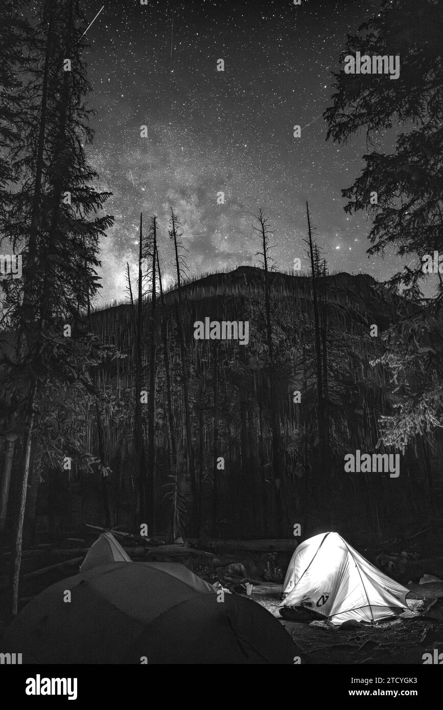 Los campings brillan suavemente bajo la impresionante Vía Láctea en el Parque Nacional de las Montañas Rocosas, proporcionando un telón de fondo perfecto para los entusiastas del cielo nocturno. Foto de stock