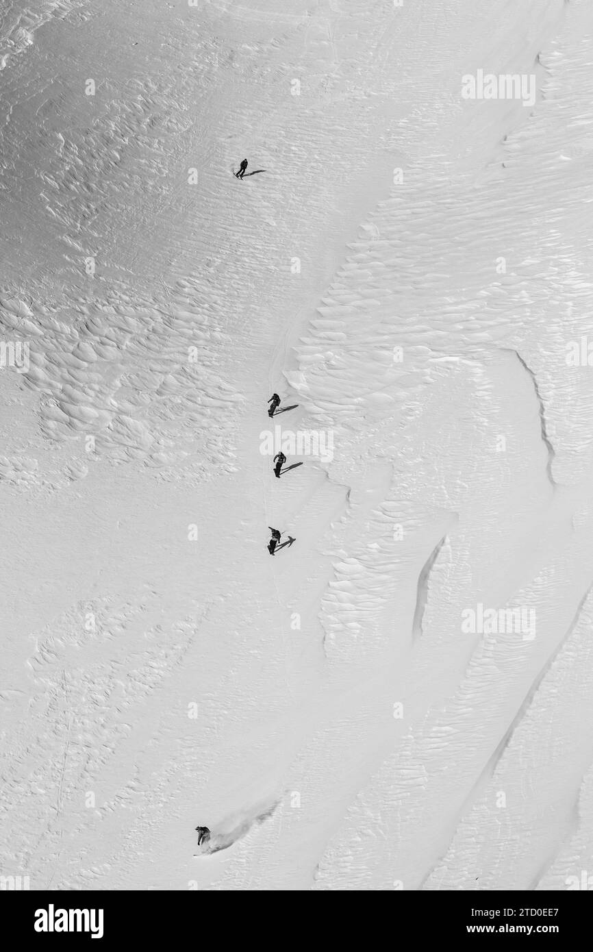 Desde arriba de un grupo irreconocible de personas montando tablas de snowboard en la majestuosa montaña nevada mientras disfruta de vacaciones en los Alpes en un día soleado Foto de stock