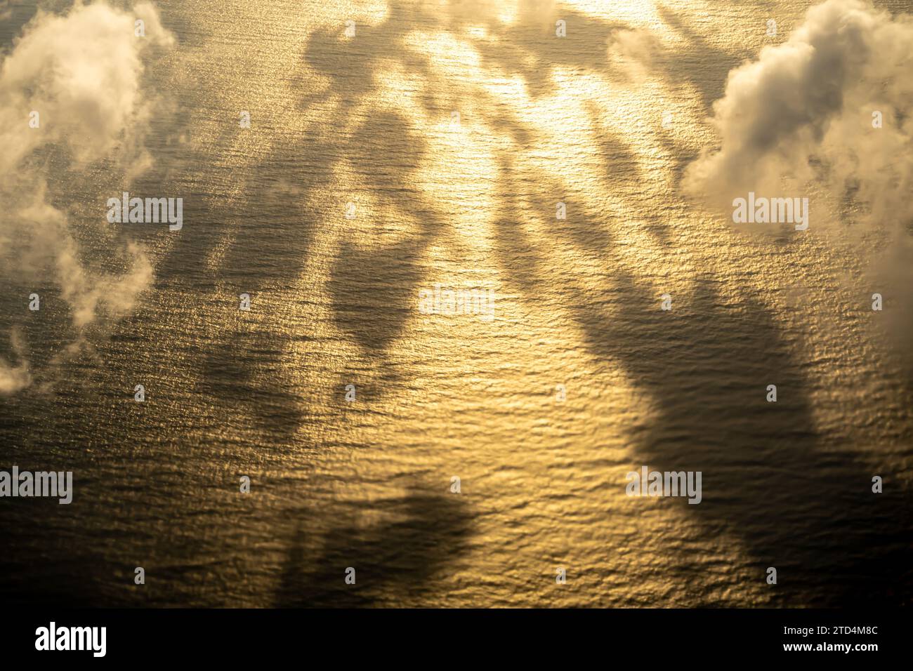 Nubes al atardecer, nubes sombras en el agua. Sombra de una nube en el mar de agua, vista de la ventana del avión del agua ondulada con rayos del sol brillando a través de las nubes Foto de stock