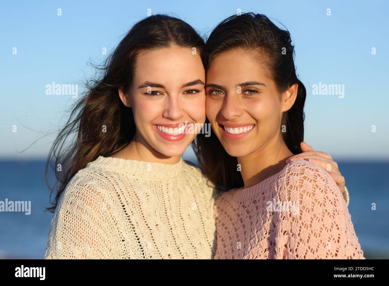 Dos mujeres felices sonriendo con sonrisas perfectas a la cámara en la playa al atardecer Foto de stock