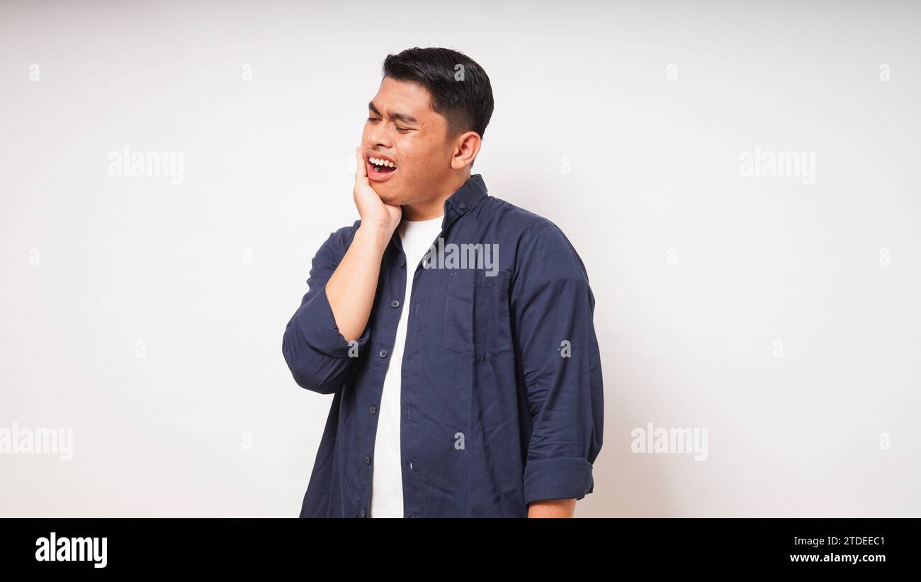 Concepto de dolor de muelas. Hombre asiático tocando su mandíbula con expresión de dolor sobre fondo blanco. toma de estudio Foto de stock