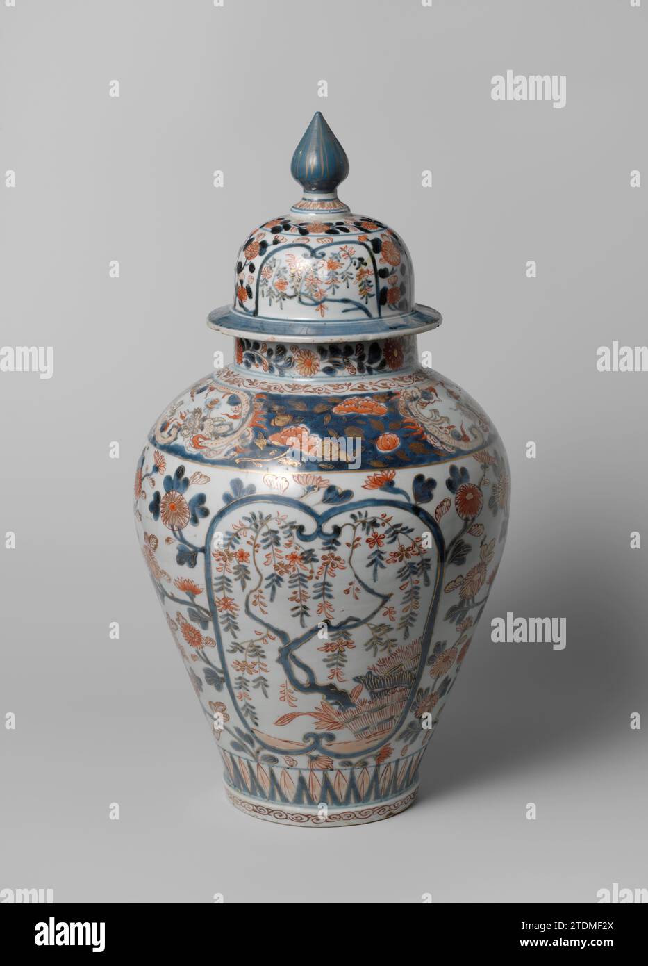 Tarro cubierto de balustre con plantas con flores, aerosoles de flores y dragones, c. 1685 - c. 1700 Tarro de tapa de porcelana en forma de balus, pintado en azul bajo esmalte y sobre el esmalte rojo y oro. En la pared tres cartoques con una planta con flores en cada uno (hortensias, peonía, wisteria) detrás de setos encuadernados. Los cartoques están rodeados de bebidas crisanthen. En el hombro un vínculo con las bebidas de peonía interrumpidas por tres perlas después de los dragones. Alrededor del pie y el cuello un neumático con rizo. Una banda con motivos de hojas elevadas y puntiagudas alrededor del pie. El cuello con crisantnums. La tapa con la misma decoración. L Foto de stock