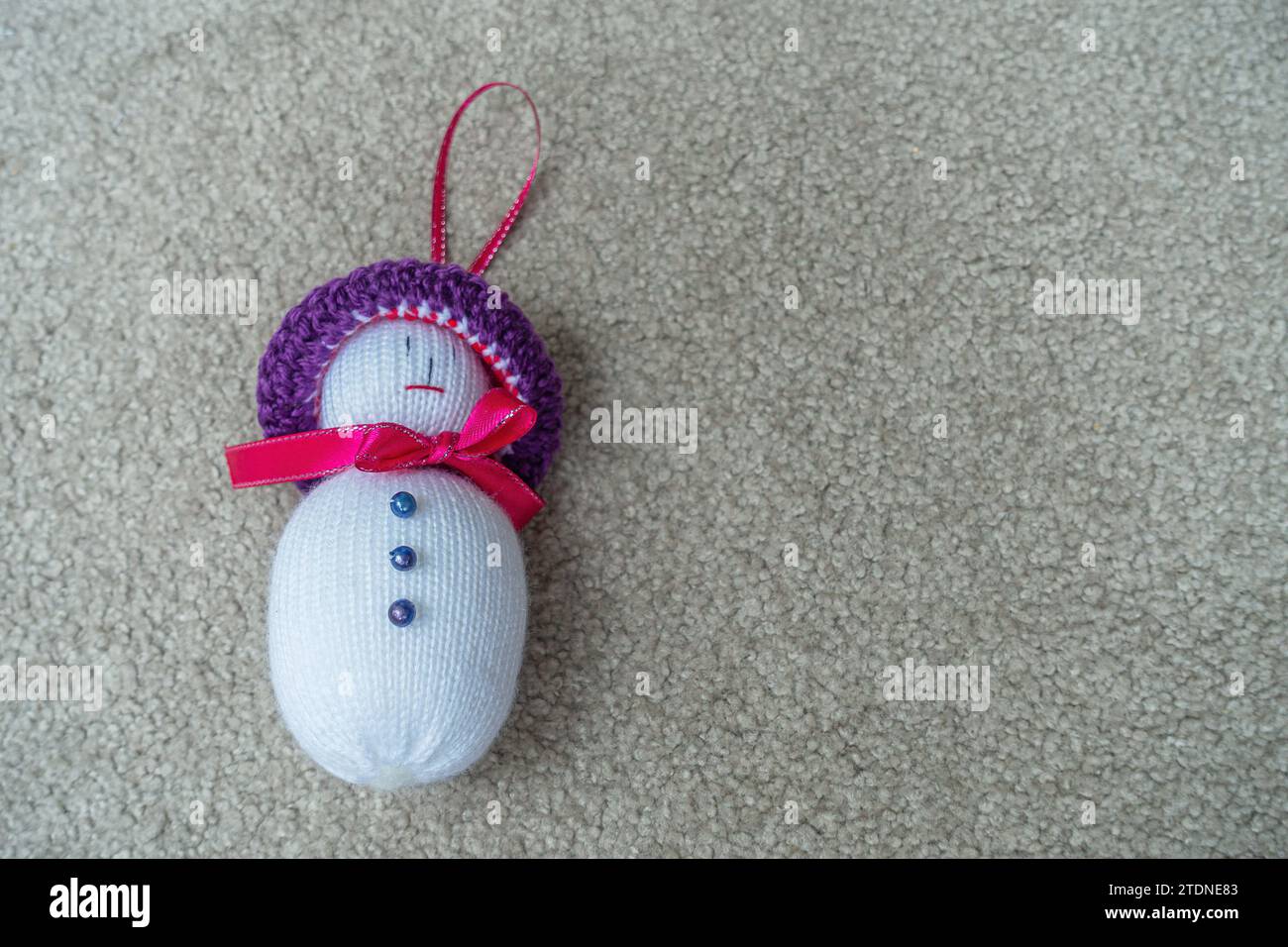 Primer plano de una pequeña muñeca de Navidad, hecha a mano en crochet, con botones, cinta y sombrero, acostado sobre una superficie de alfombra. Foto de stock