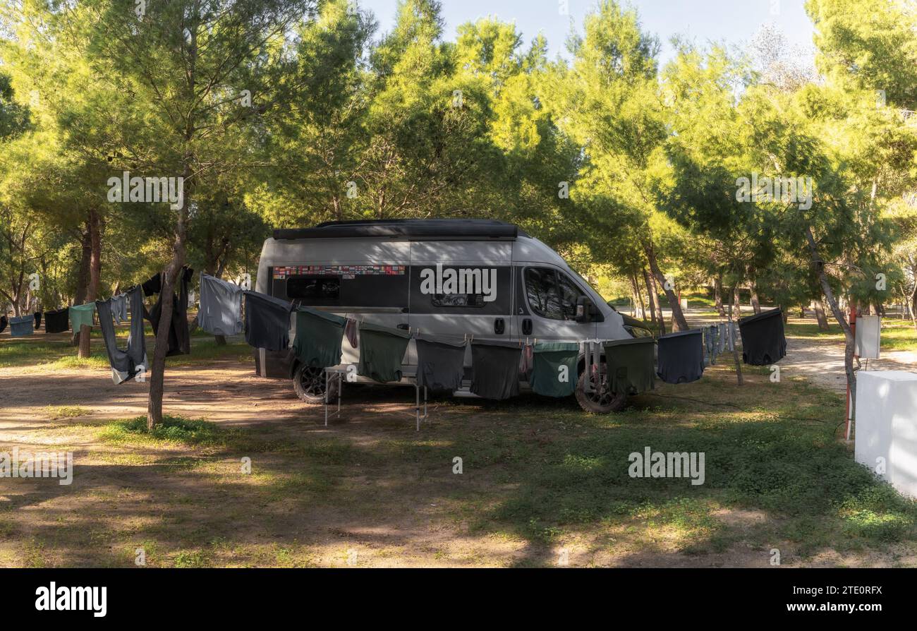 Una autocaravana gris estacionada en un campamento rodeado de árboles y ropa colgando en un tendedero en primer plano Foto de stock