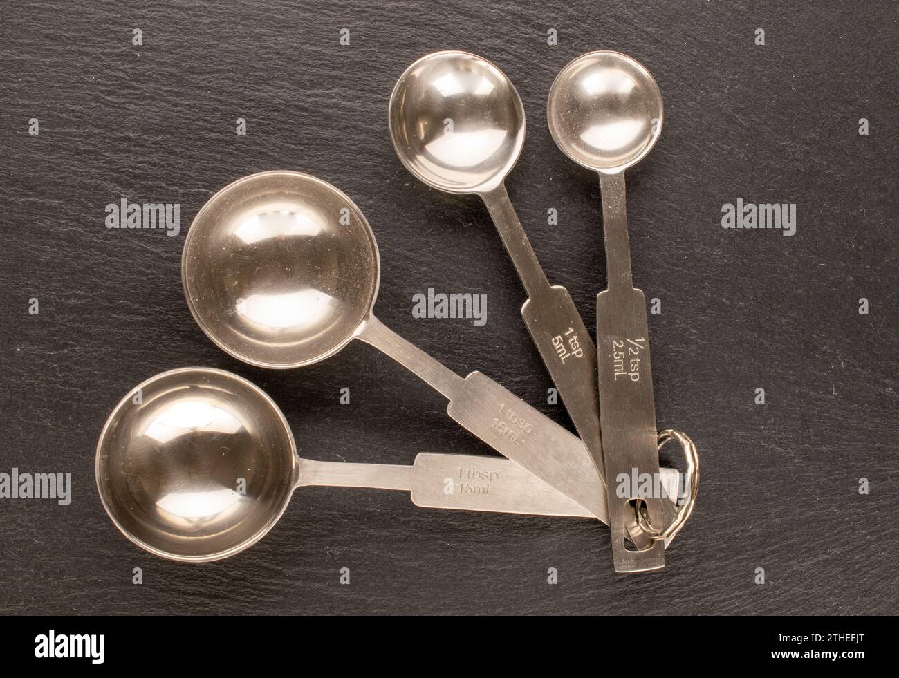 Varias cucharas de metal para medir objetos sueltos en piedra de pizarra, macro, vista superior. Foto de stock