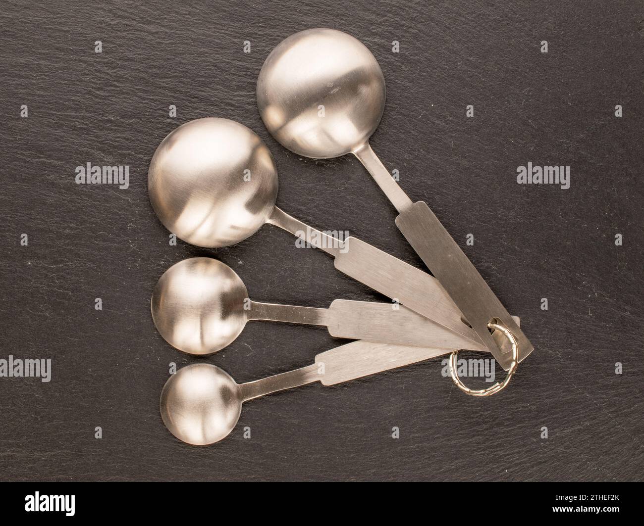 Varias cucharas de metal para medir objetos sueltos en piedra de pizarra, macro, vista superior. Foto de stock