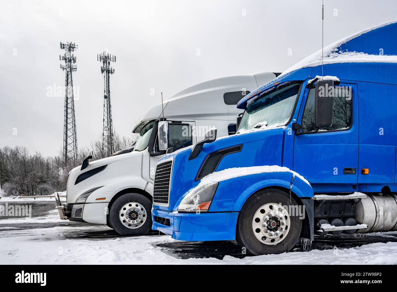 Los camiones semi-montacargas grandes con cabina alta de pie en fila en el estacionamiento medio vacío del camión del invierno para el estacionamiento con la nieve y el hielo derretido en New Hampshire New Englan Foto de stock