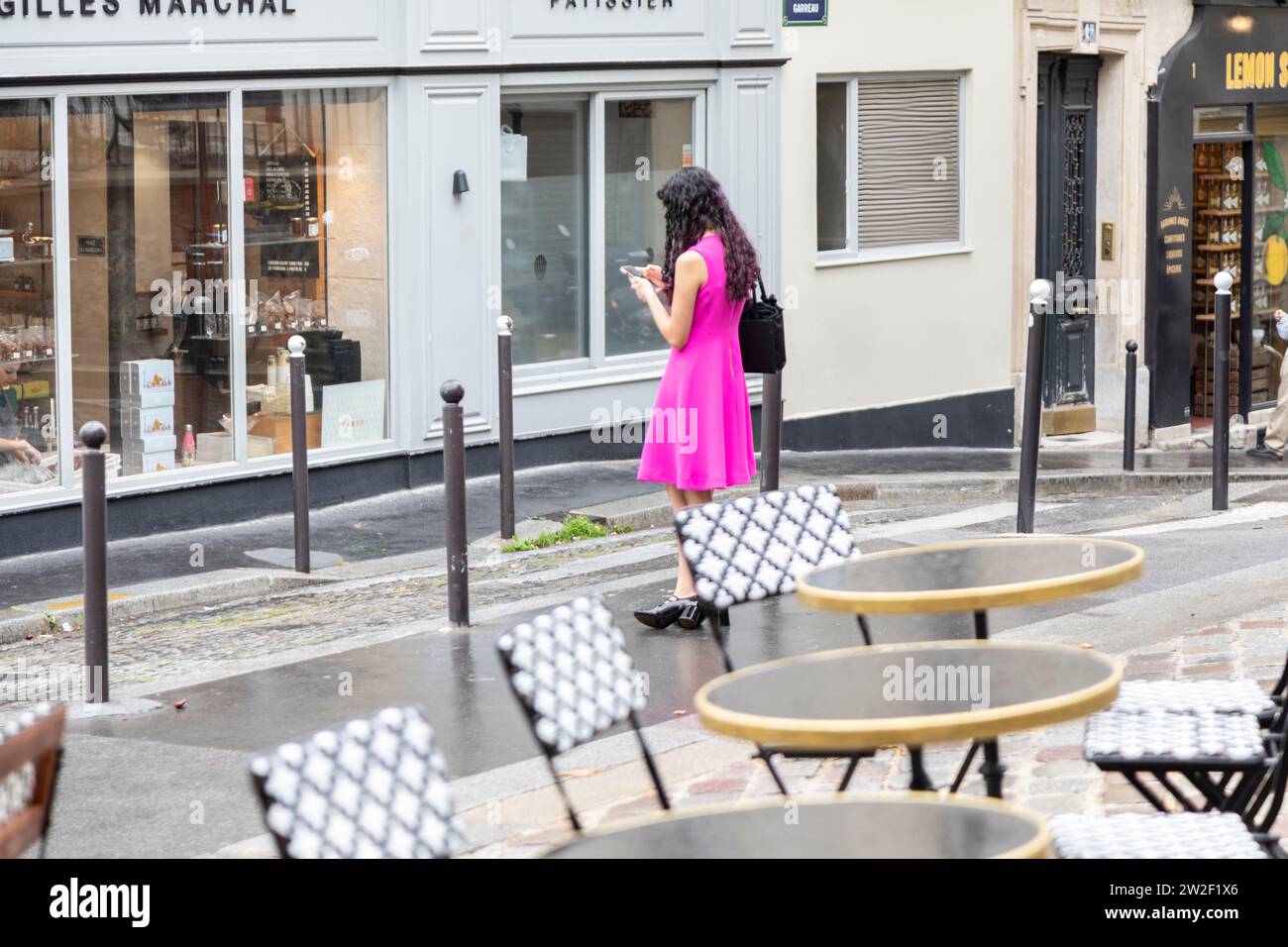 Mujer joven con vestido rosa mirando el teléfono móvil en la calle, Montmartre, París, Francia Foto de stock