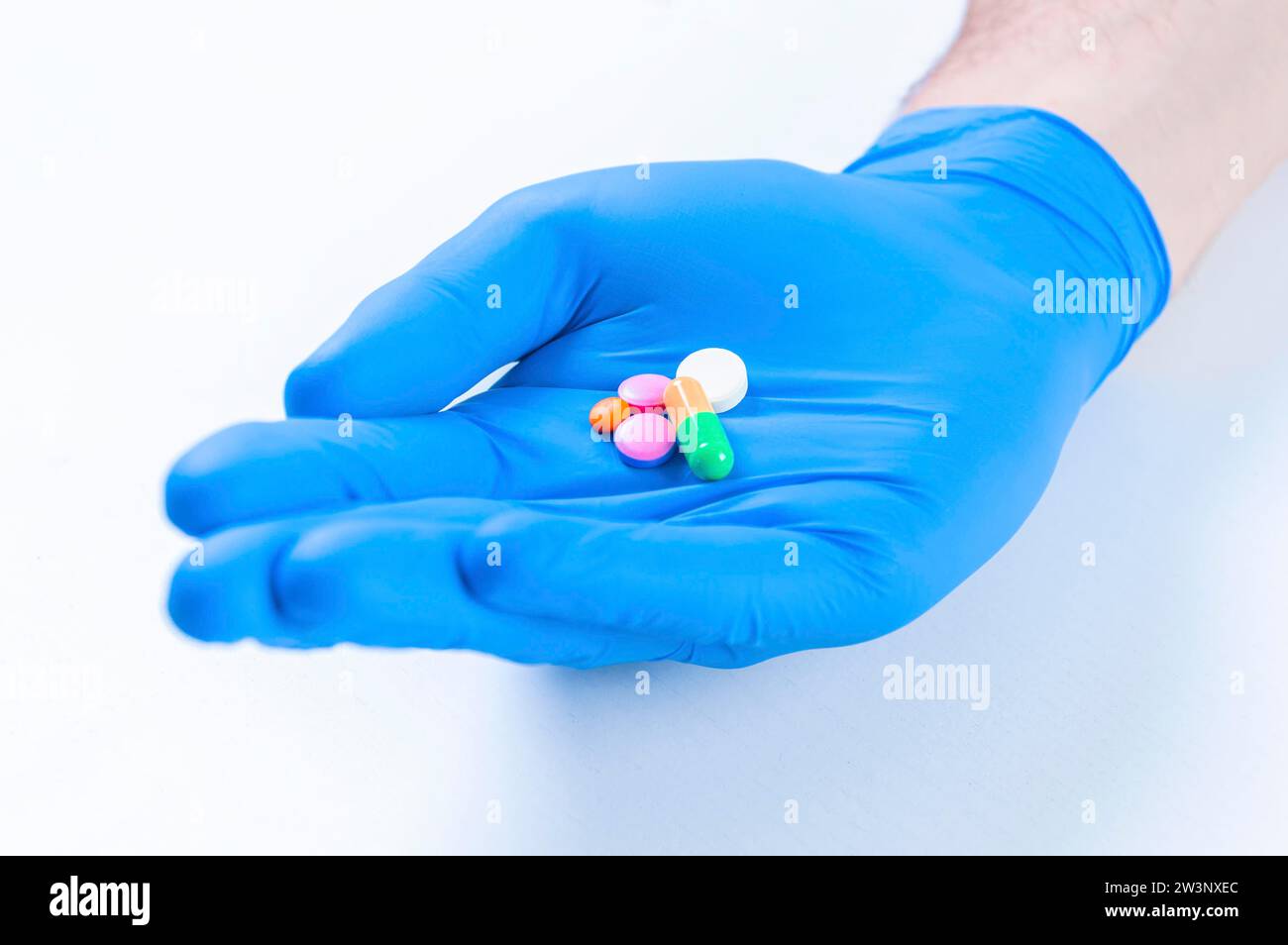 El médico sostiene las píldoras tendidas sobre un guante azul. Concepto médico. Medios mixtos Foto de stock