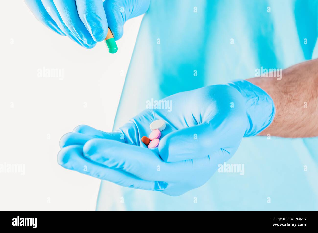 El médico sostiene las píldoras tendidas sobre un guante azul. Concepto médico. Medios mixtos Foto de stock