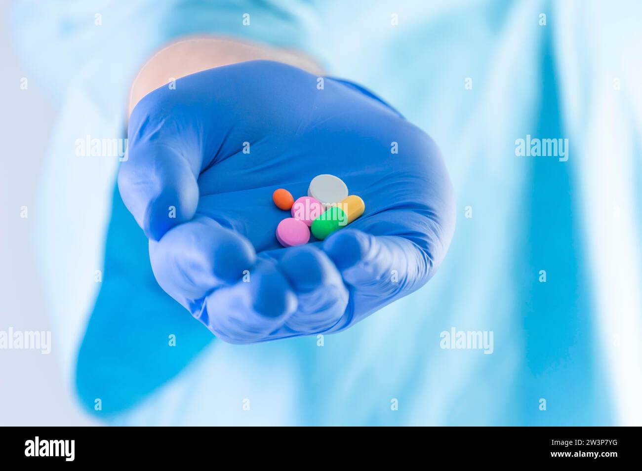 El médico sostiene las píldoras tendidas sobre un guante azul. Concepto médico. Medios mixtos Foto de stock