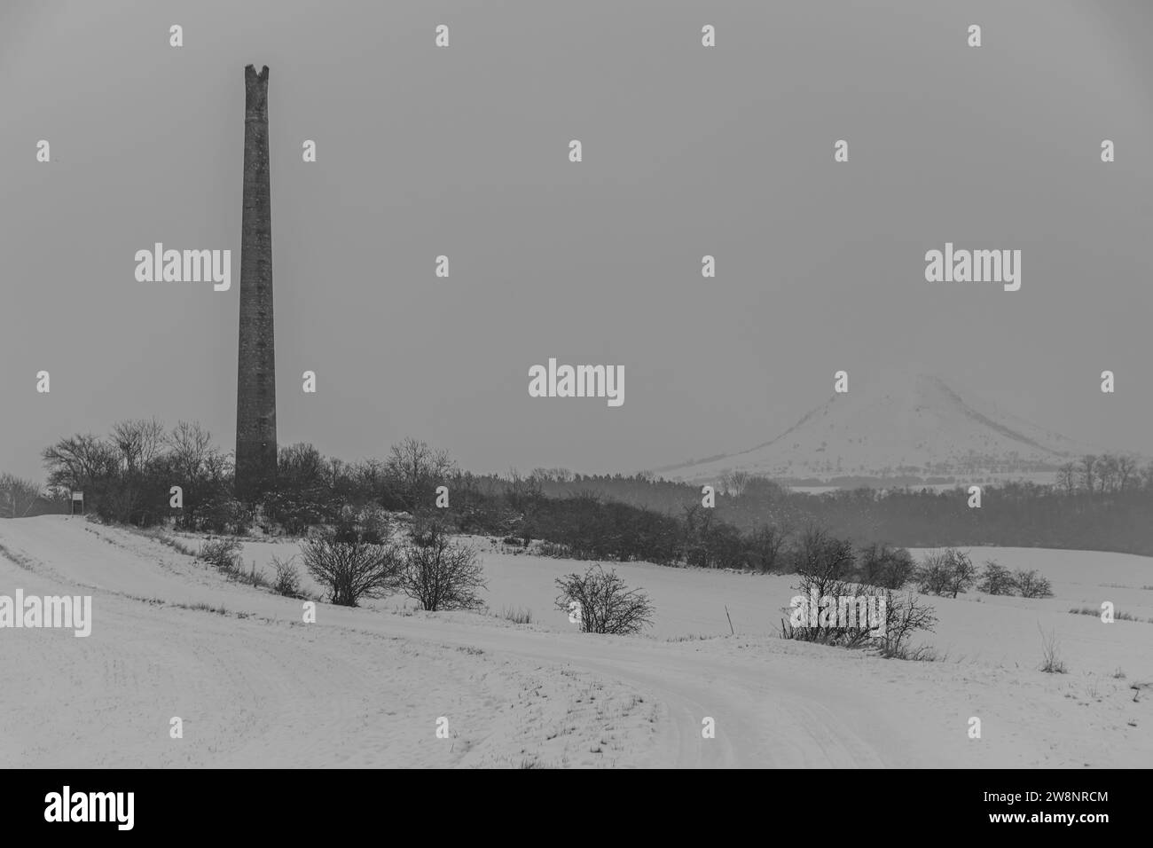 Rana hill en la mañana nevada de tormenta blanca cerca de la ciudad de Louny con antigua chimenea de ruina Foto de stock
