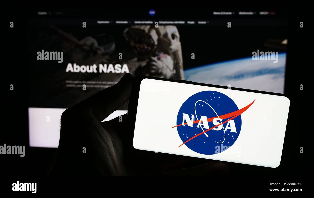 Persona que sostiene el teléfono móvil con el logotipo de la Administración Nacional de Aeronáutica y del Espacio de los Estados Unidos (NASA) en frente de la página web. Enfoque en la pantalla del teléfono. Foto de stock