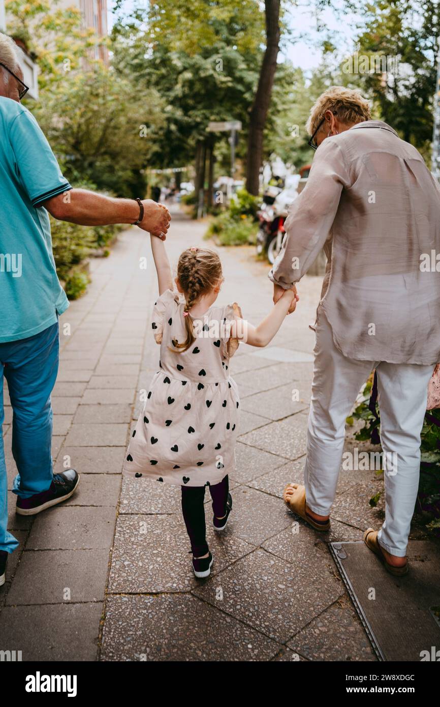 Abuelos tomados de la mano de la nieta mientras caminan por el sendero en la calle Foto de stock