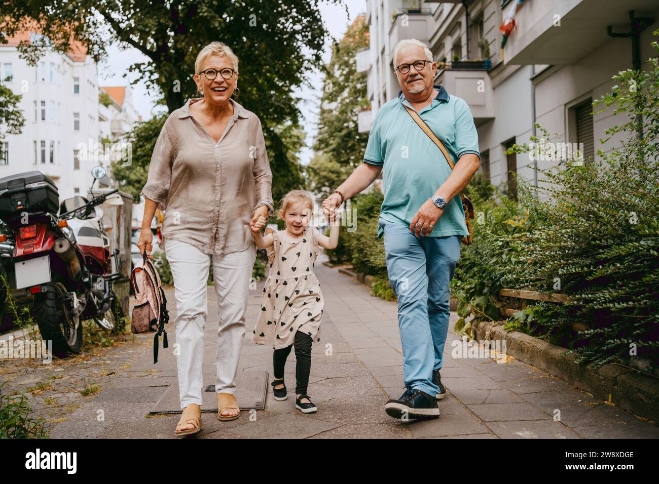 Abuelos felices tomados de la mano de la nieta mientras caminaba por la calle Foto de stock