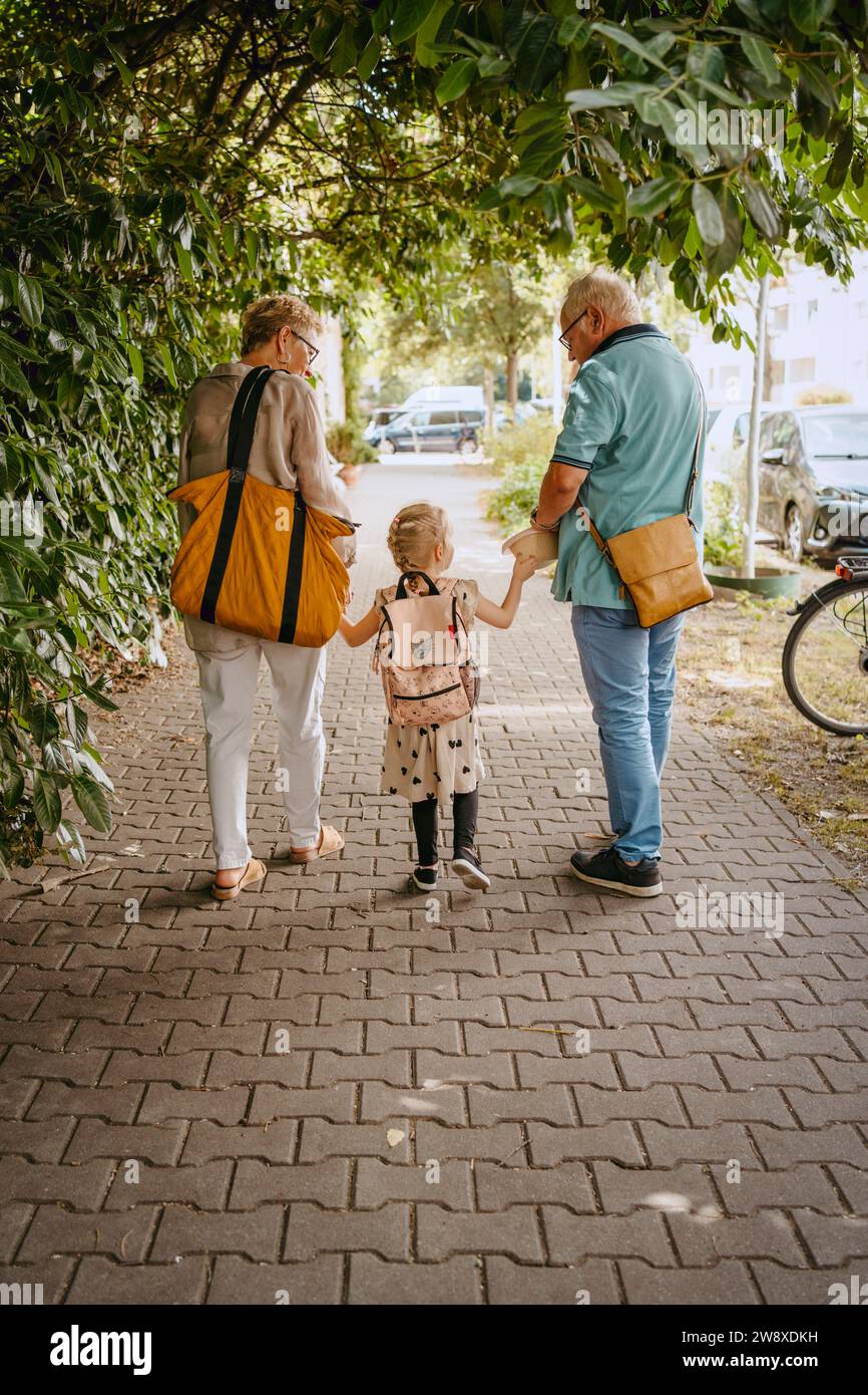 Abuelos tomados de la mano de la nieta mientras caminan por el sendero Foto de stock