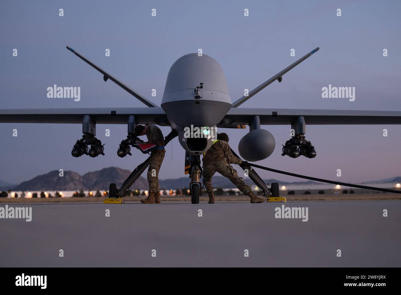 Los mantenedores de la Guardia Nacional Aérea de EE.UU. Asignados al Ala de Ataque 163d (ATKW) anotan el cable de alimentación de carga y arrastre del misil AGM-114 Hellfire al avión MQ-9 Reaper en la plataforma de carga caliente en la Base de la Reserva Aérea de Marzo en California, 10 de diciembre de 2023. La Agencia de Defensa de Misiles de los Estados Unidos llevó a cabo una interceptación exitosa de un misil balístico de alcance intermedio (IRBM) por un Interceptor Basado en Tierra (GBI) mejorado. La prueba demostró la capacidad de la defensa de curso medio (GMD) basada en tierra para atacar las amenazas más rápido. El 163d ATKW se encargó de ayudar al lanzamiento mediante la localización del cohete caído Foto de stock