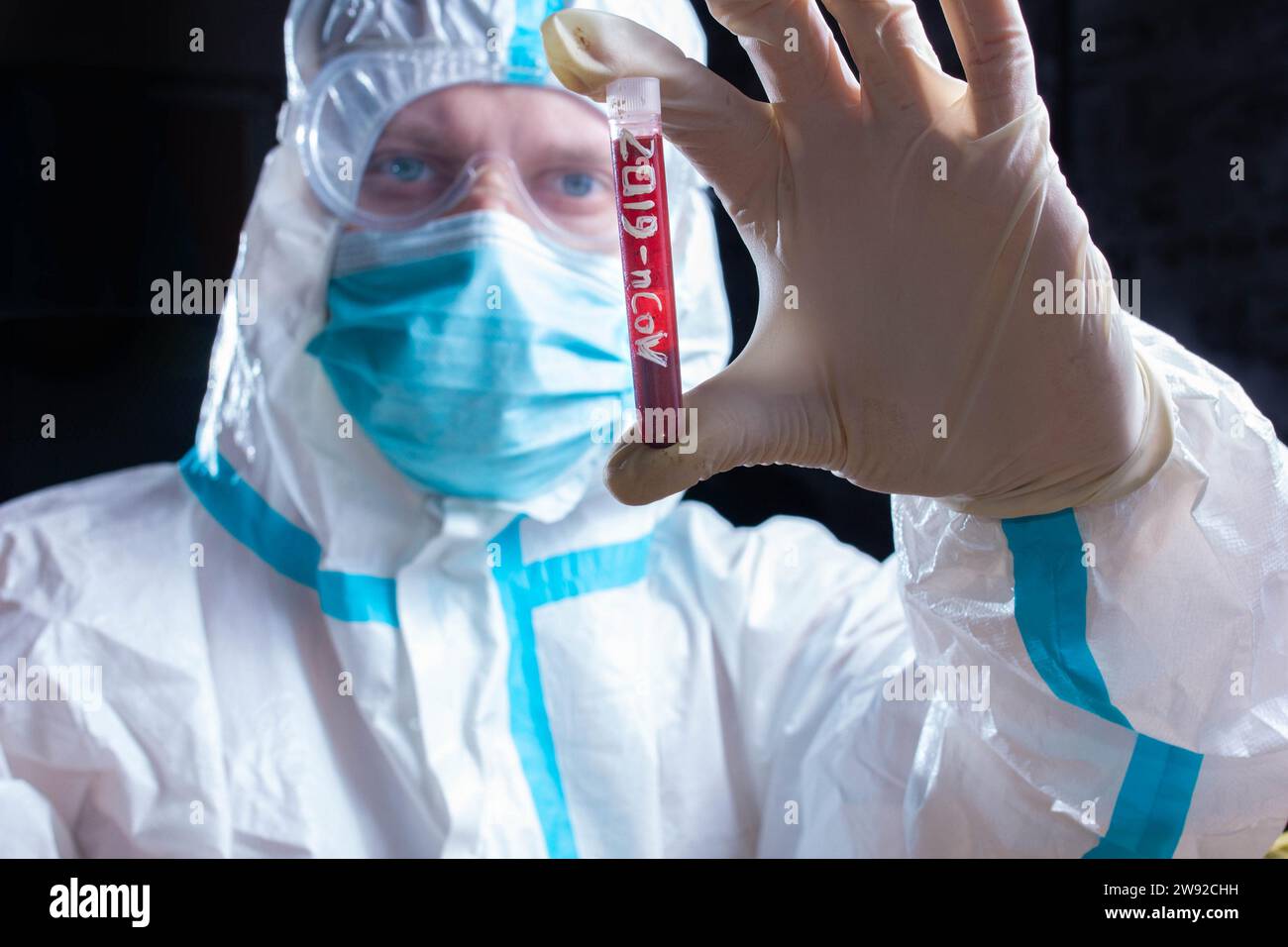 Médico asistente de laboratorio en equipo de protección personal contra el coronavirus sostiene un tubo de prueba con sangre para realizar una prueba de COVID 19 Foto de stock