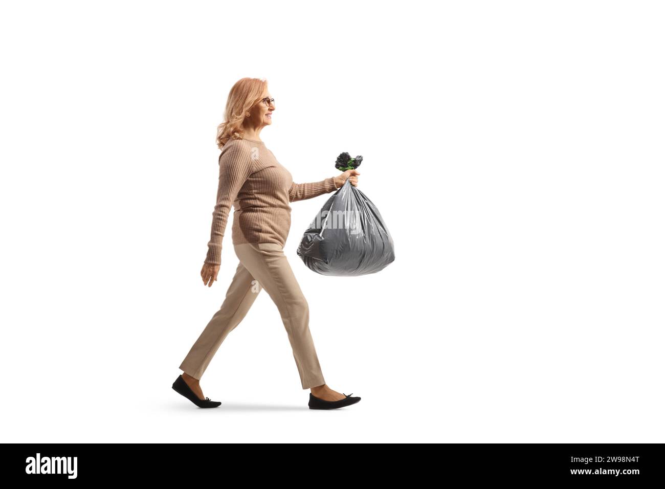 Foto de perfil de longitud completa de una mujer de mediana edad que lleva una bolsa de residuos de plástico aislada sobre fondo blanco Foto de stock