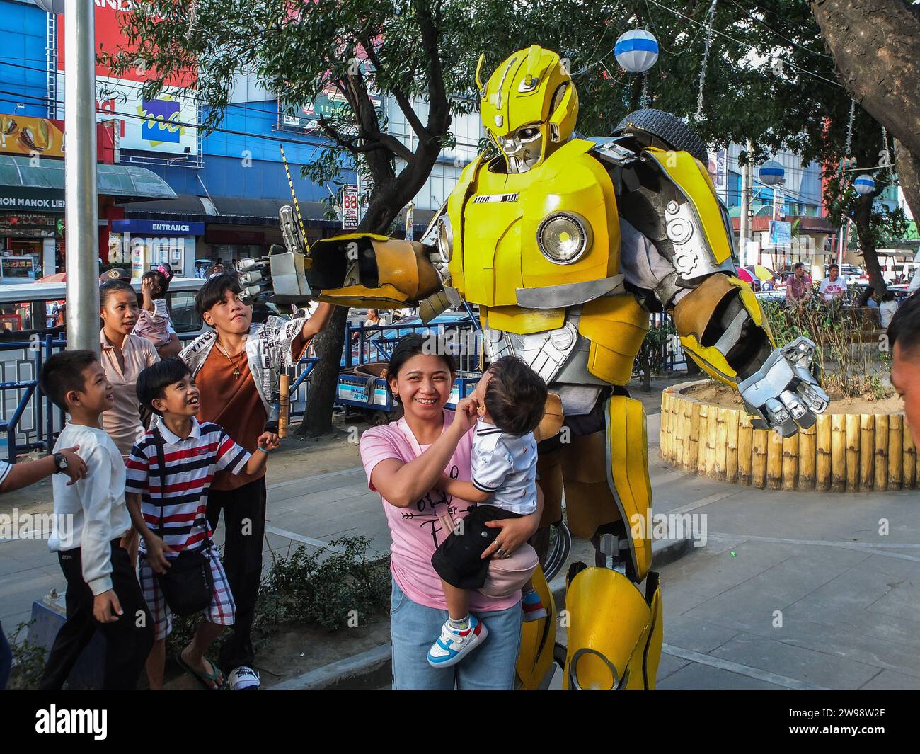 Ciudad de Malabon, Filipinas. 25 de diciembre de 2023. Una madre y su hijo posan para una foto con Bumblebee el día de Navidad. Un encuentro y saludo con la actividad de foto op se llevó a cabo en Paskuhan Village en la ciudad de Malabon. Basado en el personaje de la película transformador estadounidense Bumblebee, se llevó a cabo un encuentro y saludo con actividad de foto op en Paskuhan Village en la ciudad de Malabon. Su creador de vestuario Ardam Sexmoan dijo que les encanta actuar para que los niños sean felices este día de Navidad. (Foto de Josefiel Rivera/SOPA Images/Sipa USA) Crédito: SIPA USA/Alamy Live News Foto de stock